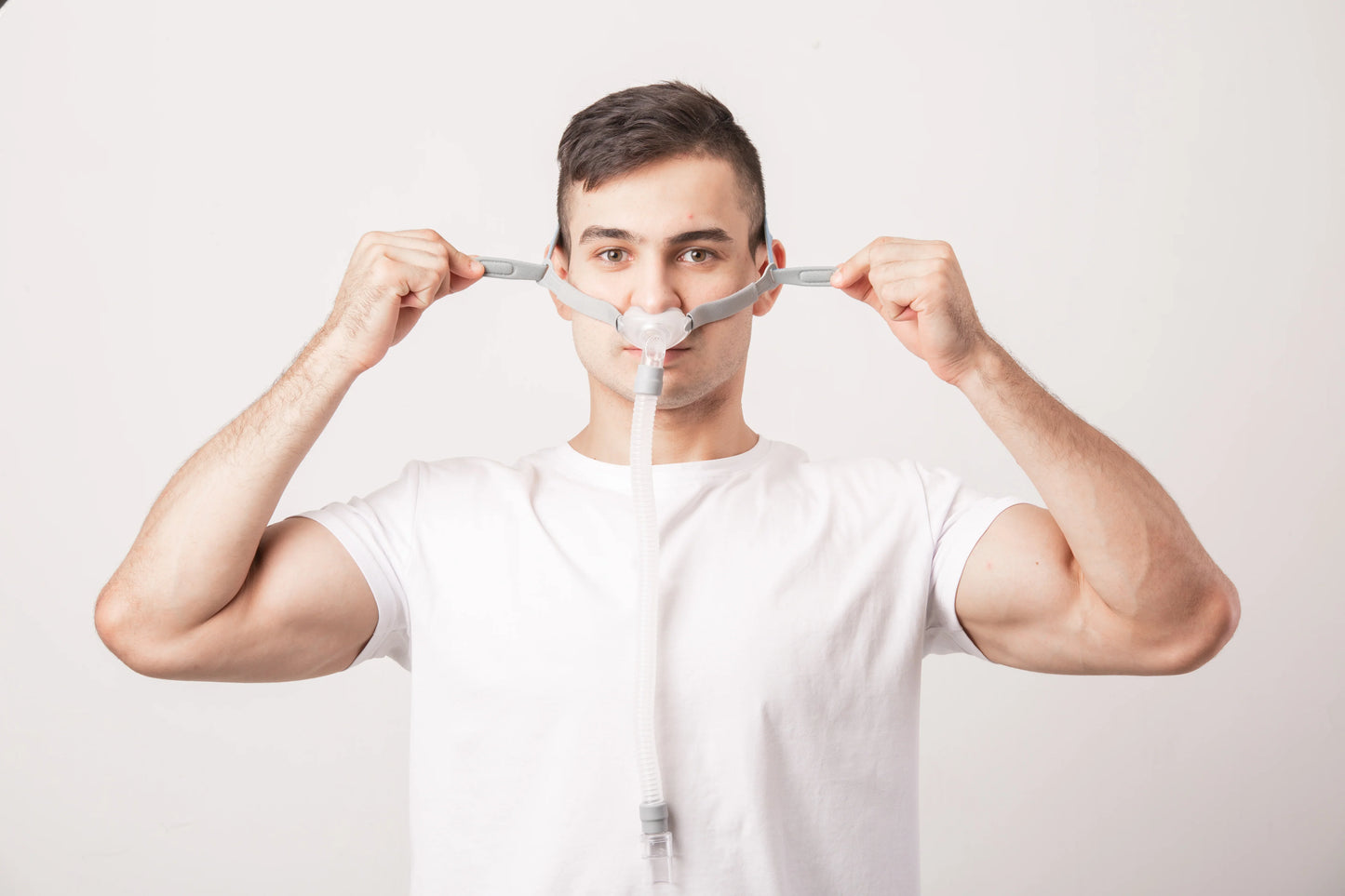Man wearing nasal CPAP mask for sleep apnea therapy on white background