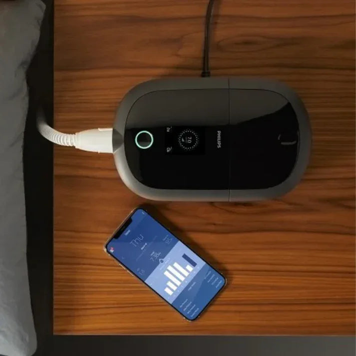 CPAP machine with digital display on wooden nightstand beside smartphone sleep app