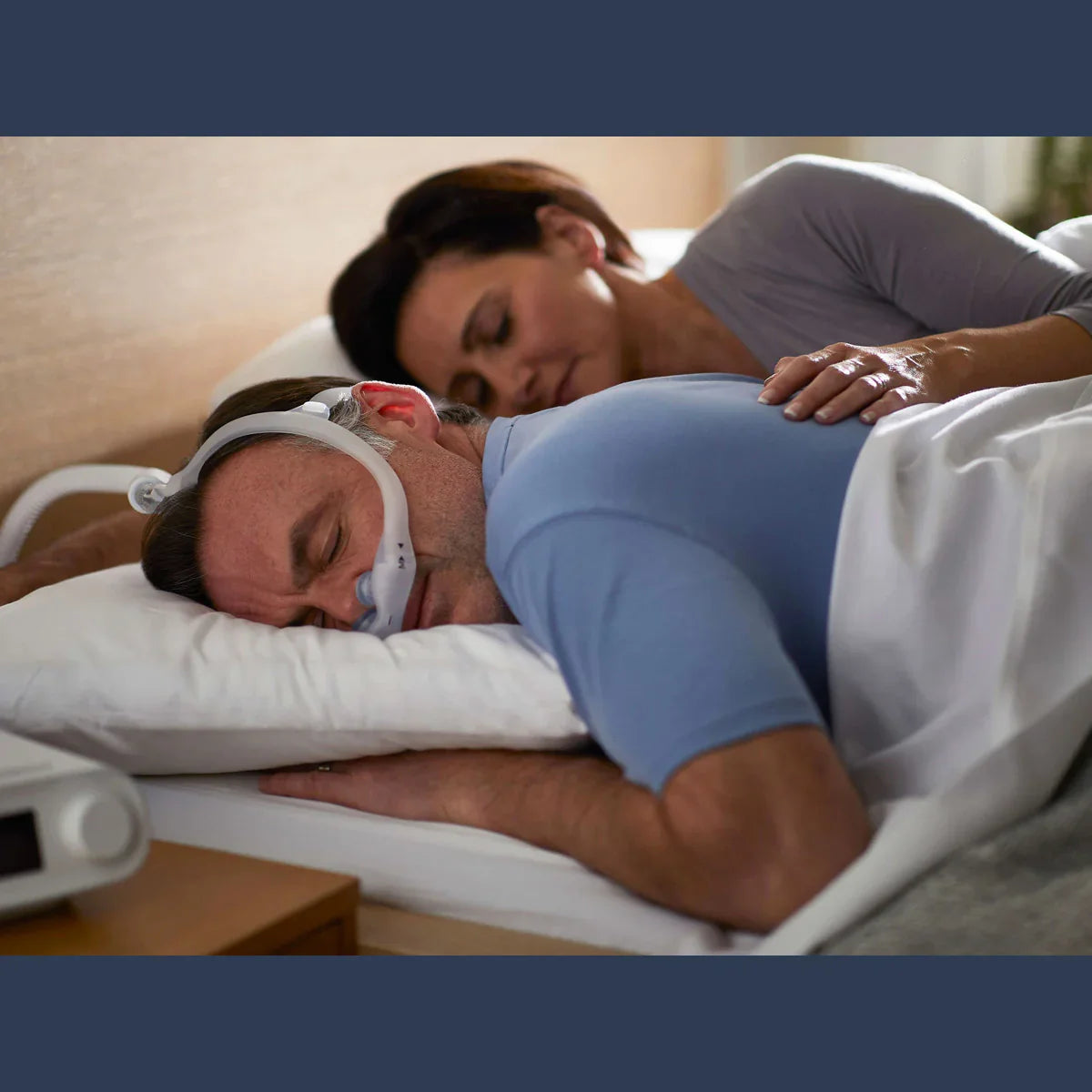 Man sleeping with nasal CPAP mask and gel pillows, lying on side in bed