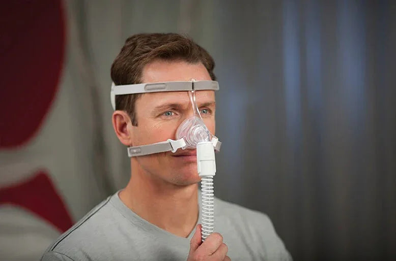 Man wearing CPAP nasal mask with headgear and hose for sleep apnea therapy