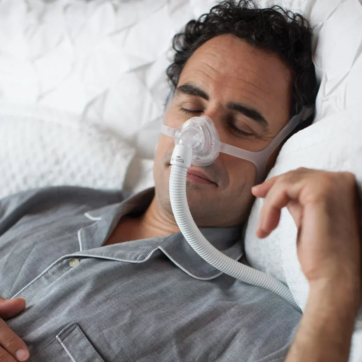Man sleeping in bed wearing CPAP nasal mask for sleep apnea therapy