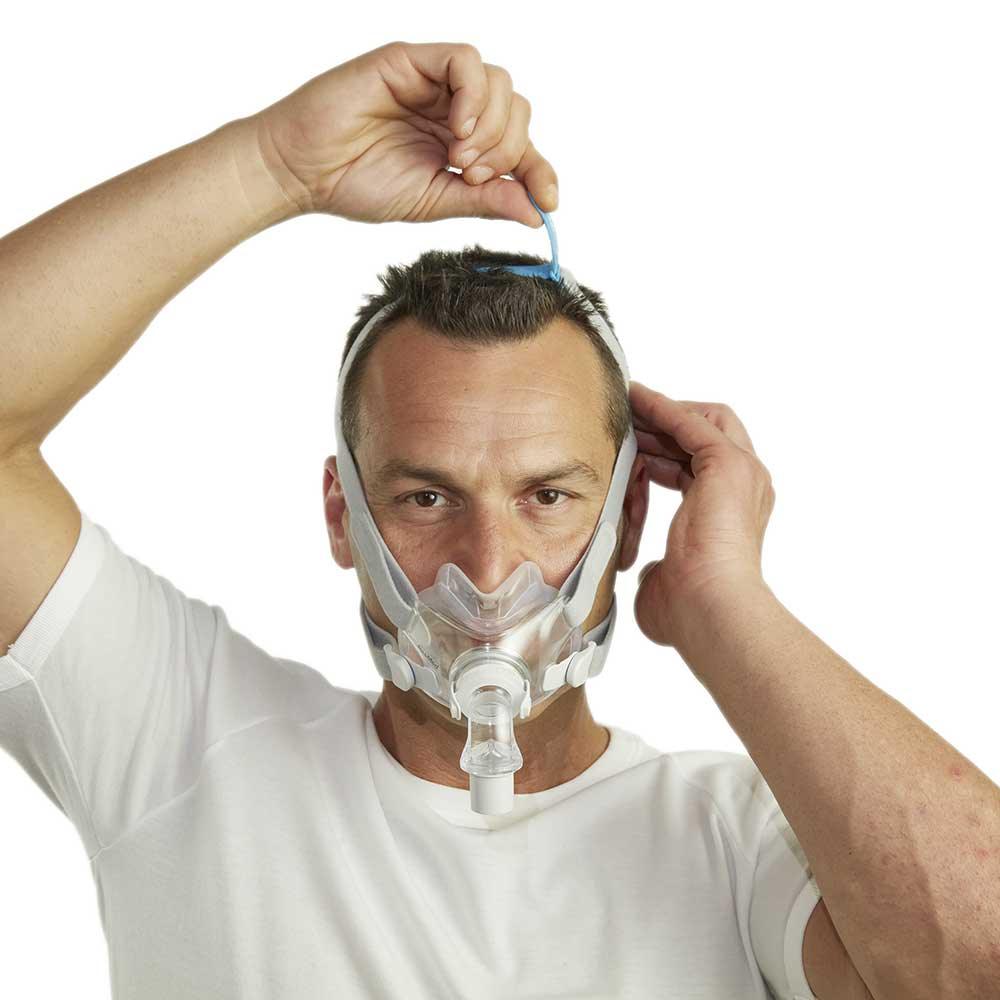 Man adjusting full face CPAP mask for sleep apnea therapy on white background
