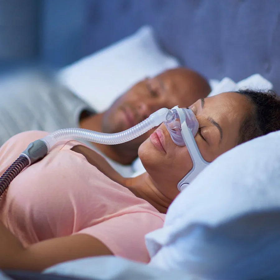 Woman sleeping with nasal CPAP mask and hose for sleep apnea therapy in bed