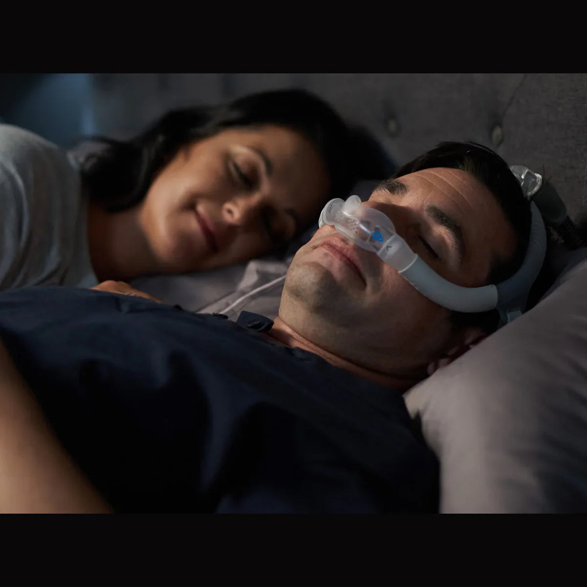 Man sleeping with nasal CPAP mask in bed, sleep apnea therapy, partner beside him