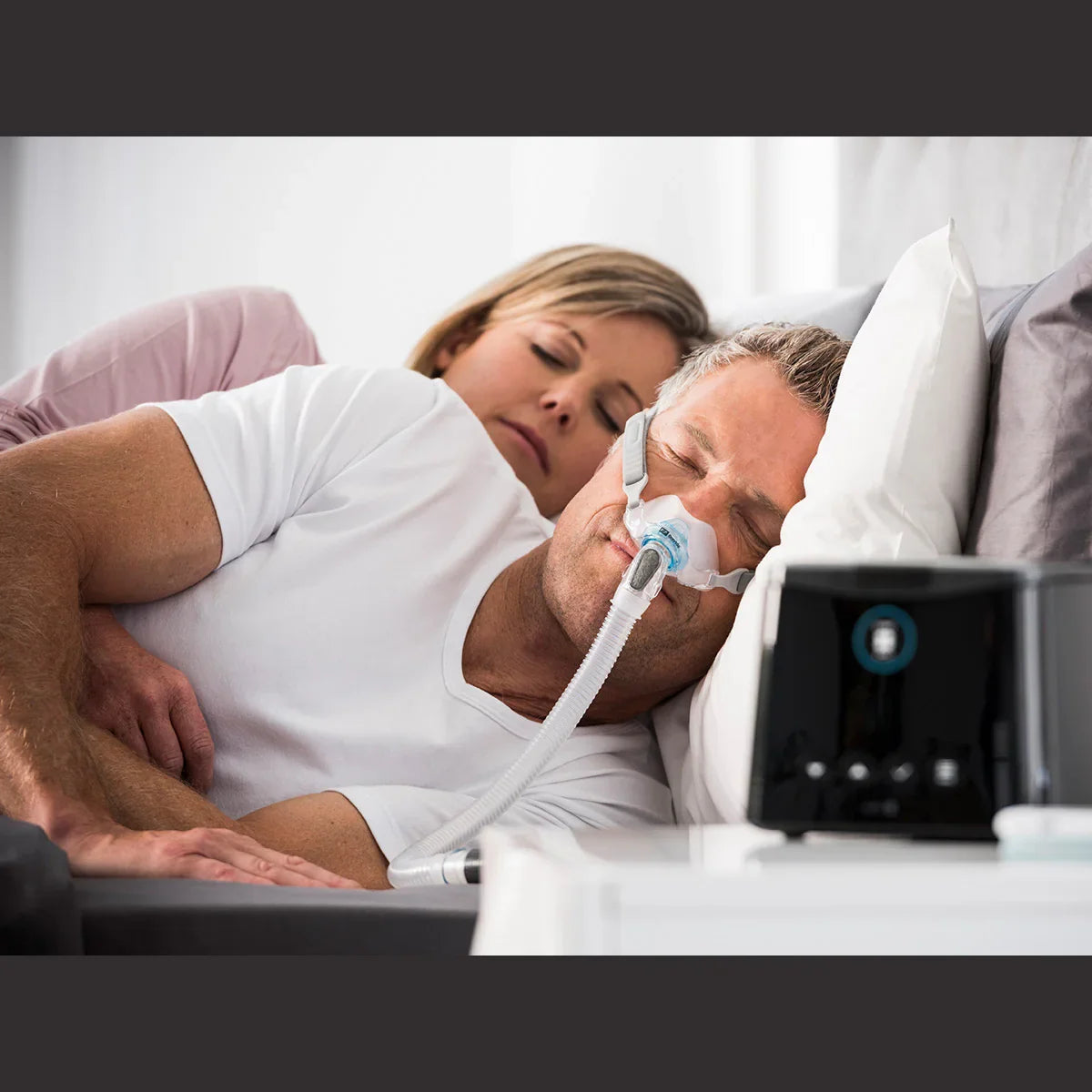 Man sleeping with nasal pillow CPAP mask connected to auto CPAP machine in bedroom