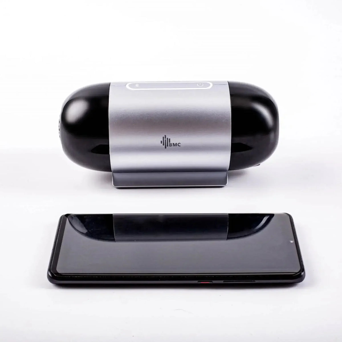 A black and silver CPAP device with a central metallic band and a visible 'BMC' logo, shown above a black smartphone on a clean white background.