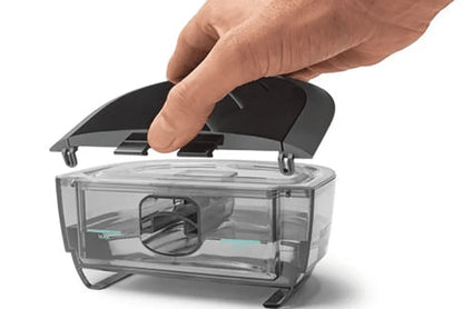 Hand opening the black lid of a transparent CPAP humidifier water chamber.