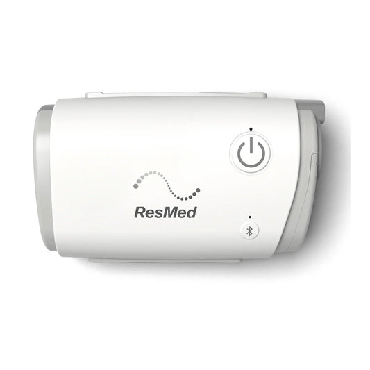 A white ResMed Travel CPAP device with gray side panels, featuring a power button and Bluetooth symbol on the front, set against a plain white background.