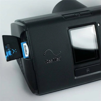 A close-up of a black ResMed CPAP Machine showing the side panel open to reveal a blue-and-white ResMed brand card or module inserted into a side port.