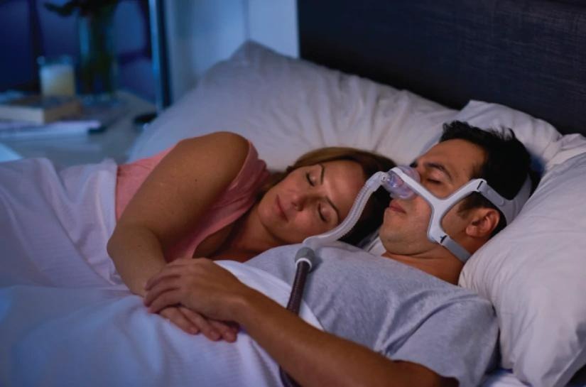 Man sleeping with CPAP mask in bed, woman beside him, peaceful night sleep scene
